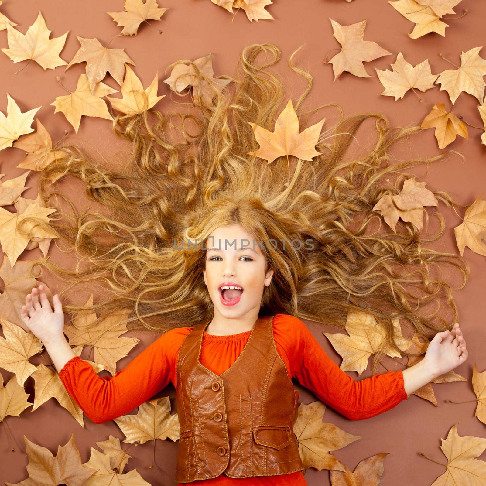 autumn fall little blond girl on dried tree leaves background and long spread hair