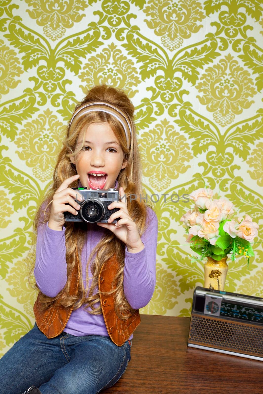 hip retro little girl shooting photo with vintage camera on wallpaper