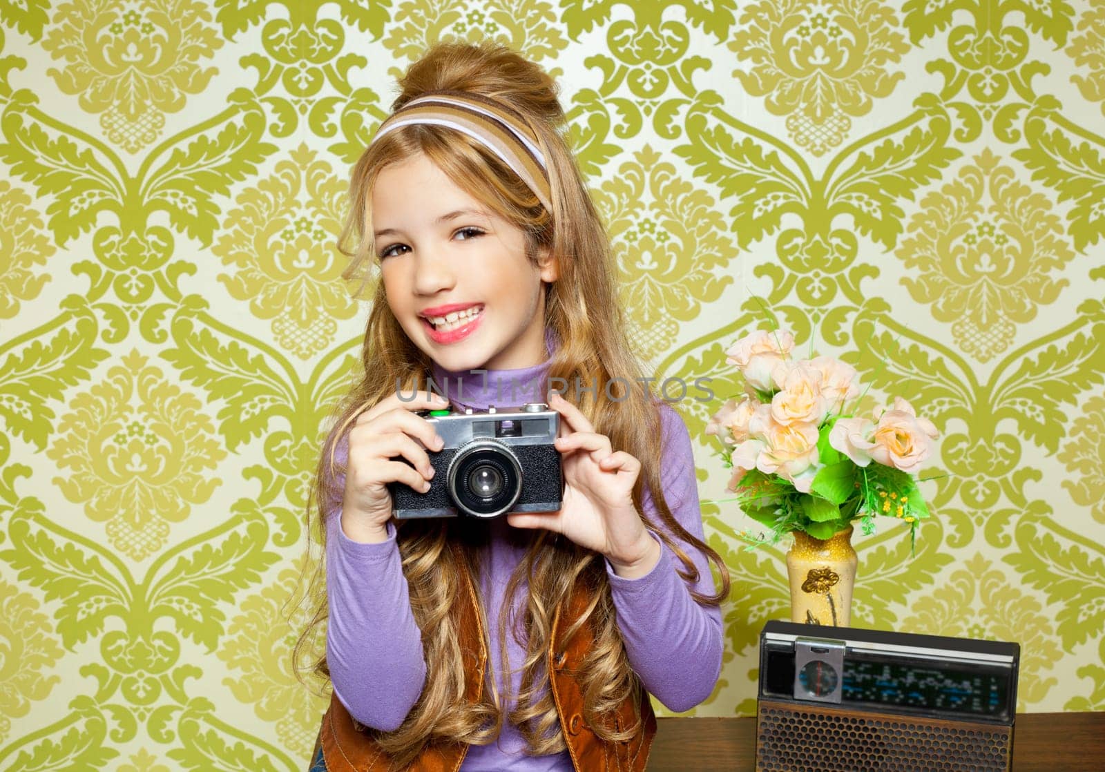 hip retro little girl shooting photo with vintage camera on wallpaper