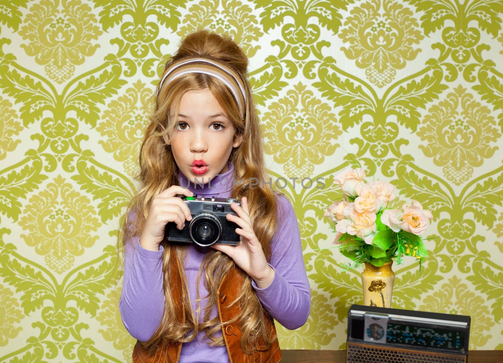 hip retro little girl shooting photo with vintage camera on wallpaper
