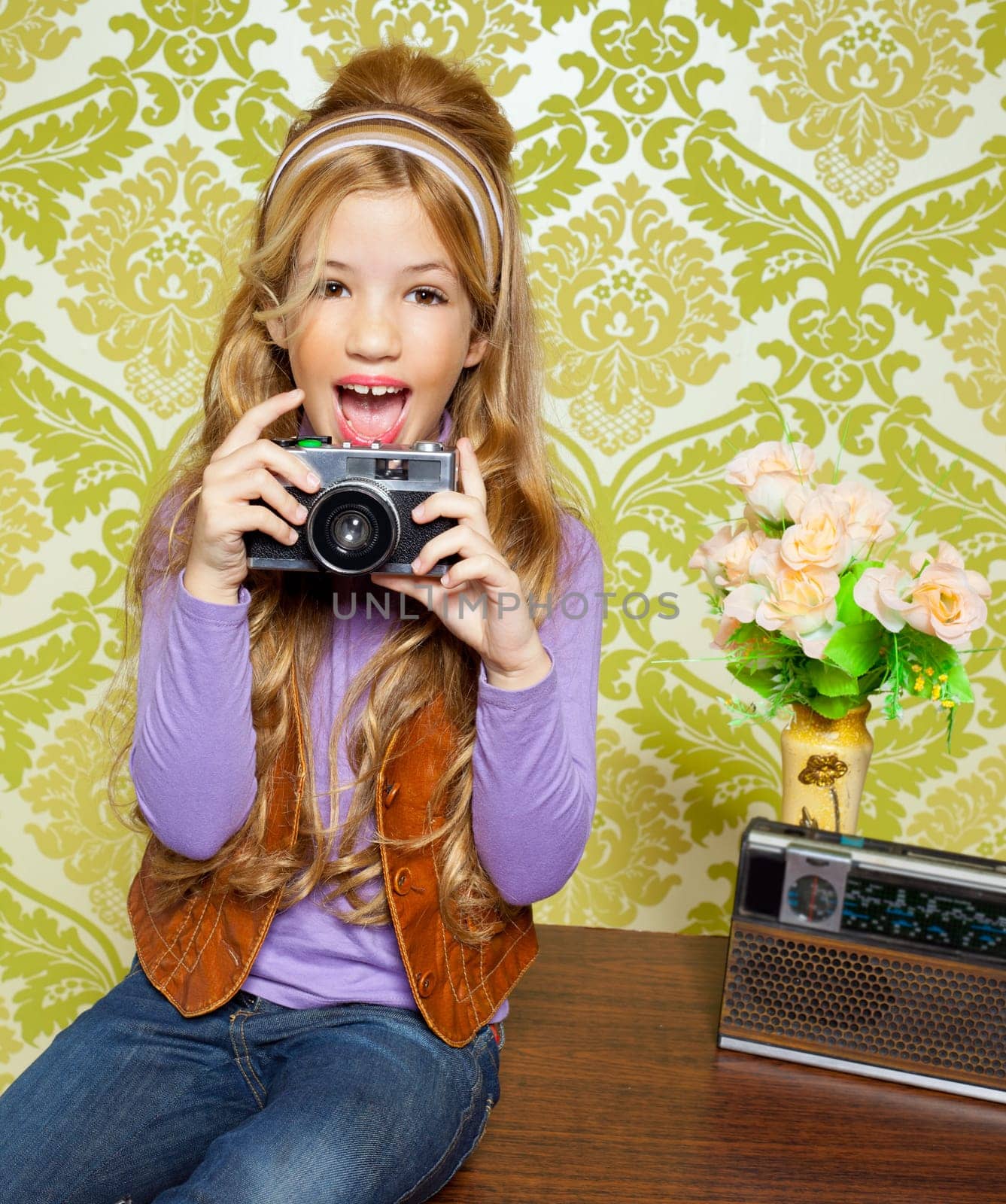 hip retro little girl shooting photo with vintage camera on wallpaper