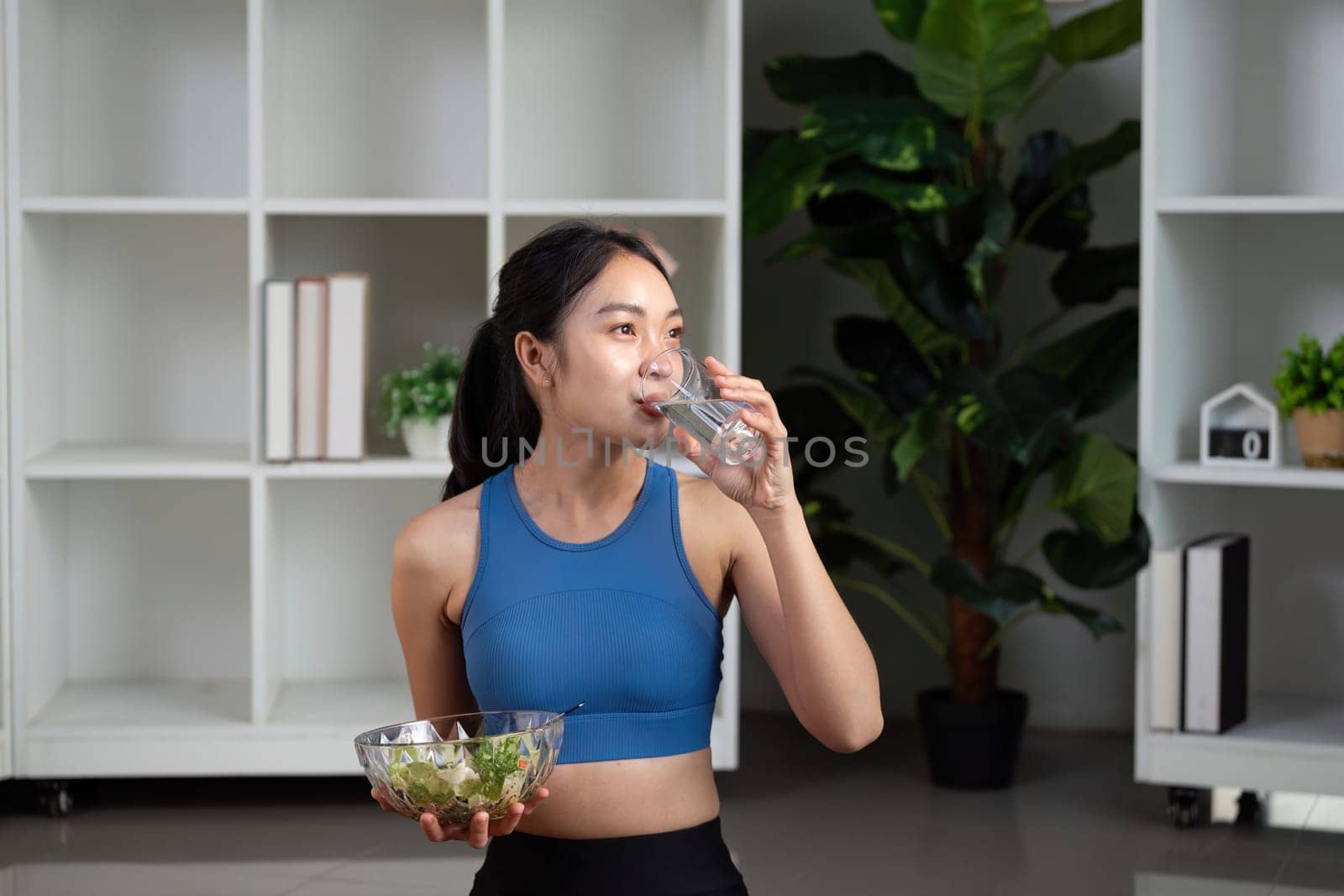 A woman takes a sip of water while holding a salad, emphasizing the importance of hydration in a healthy diet.