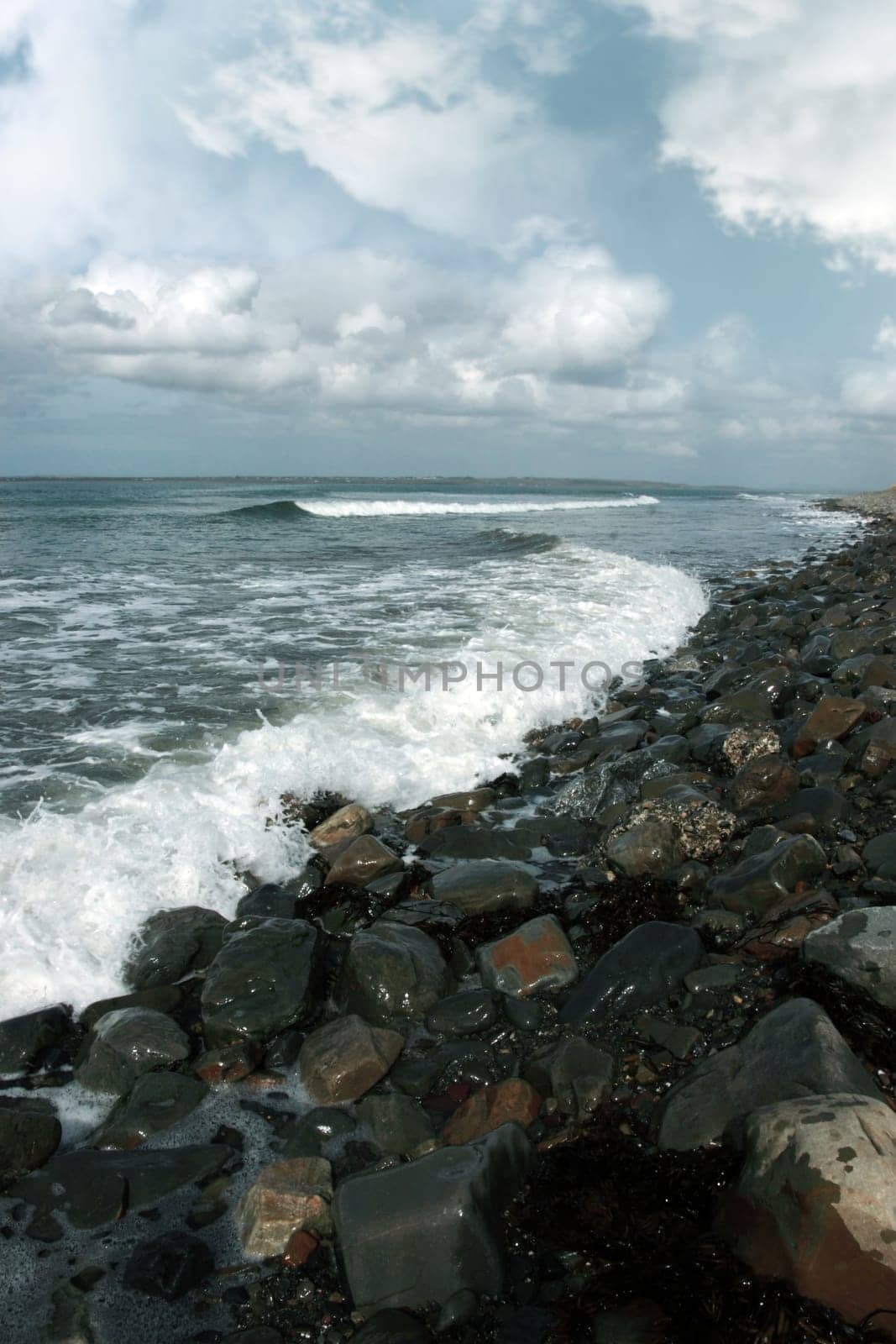 a pebbled beach on a bright day with calm sea waves splashing against the pebbles as a background