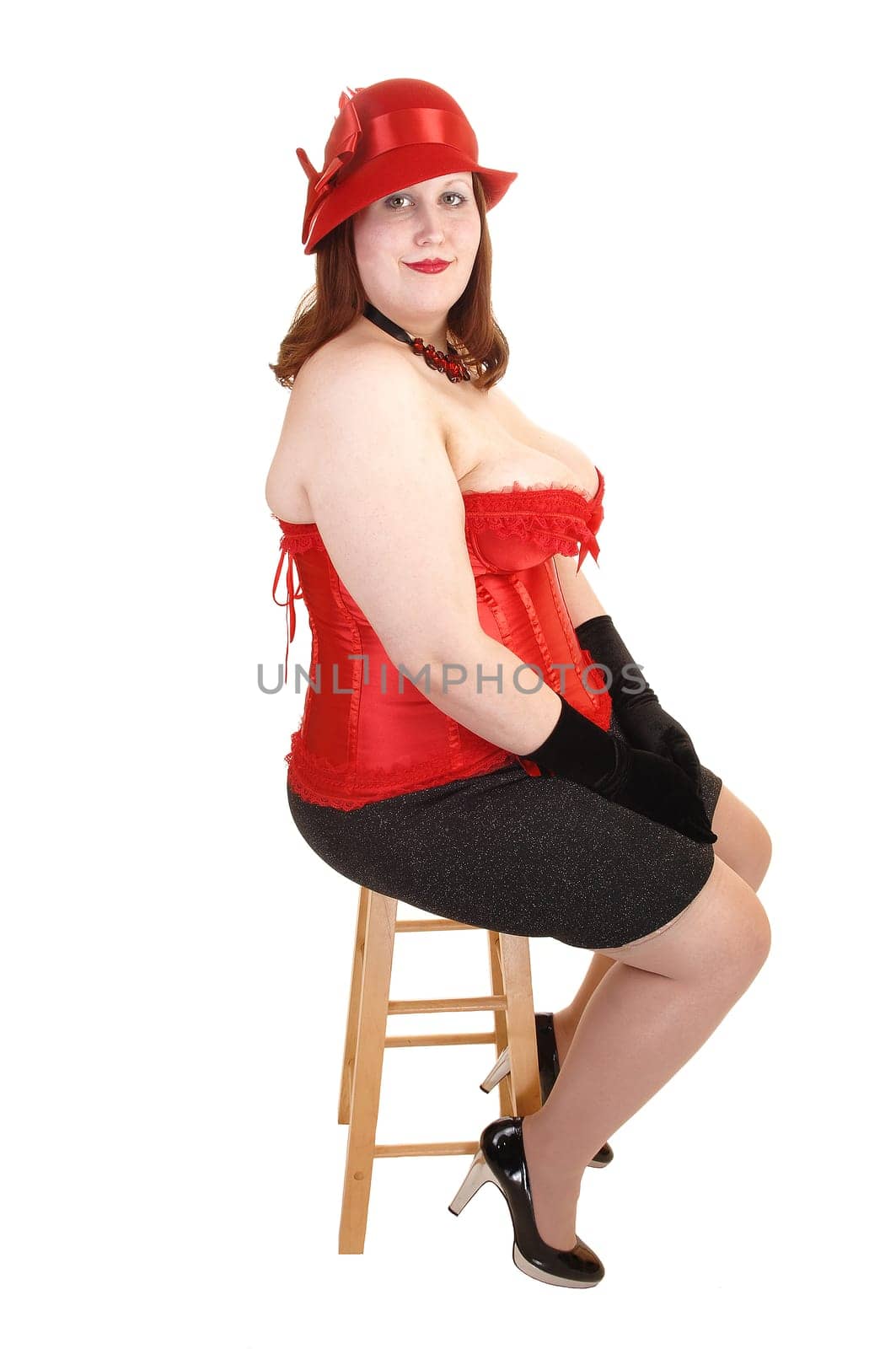 A young pretty woman in a gray skirt and red corset and hat, sitting on a chair showing her big overweight bode, for white background.