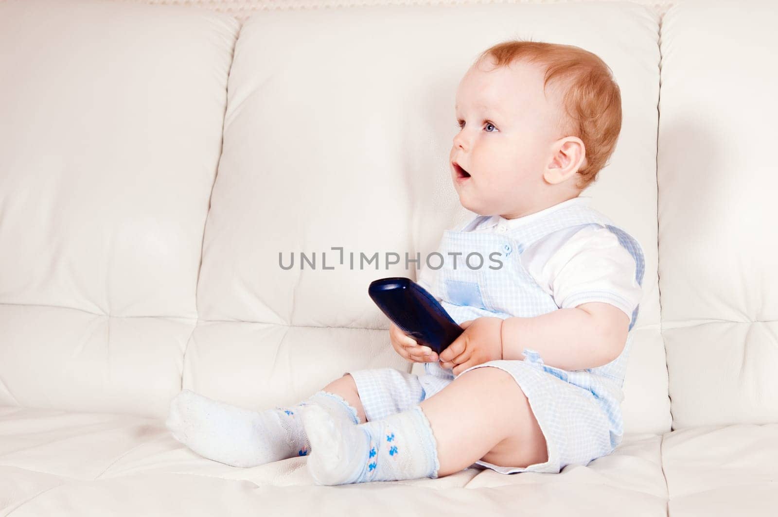 The baby sits on a white sofa with the TV panel