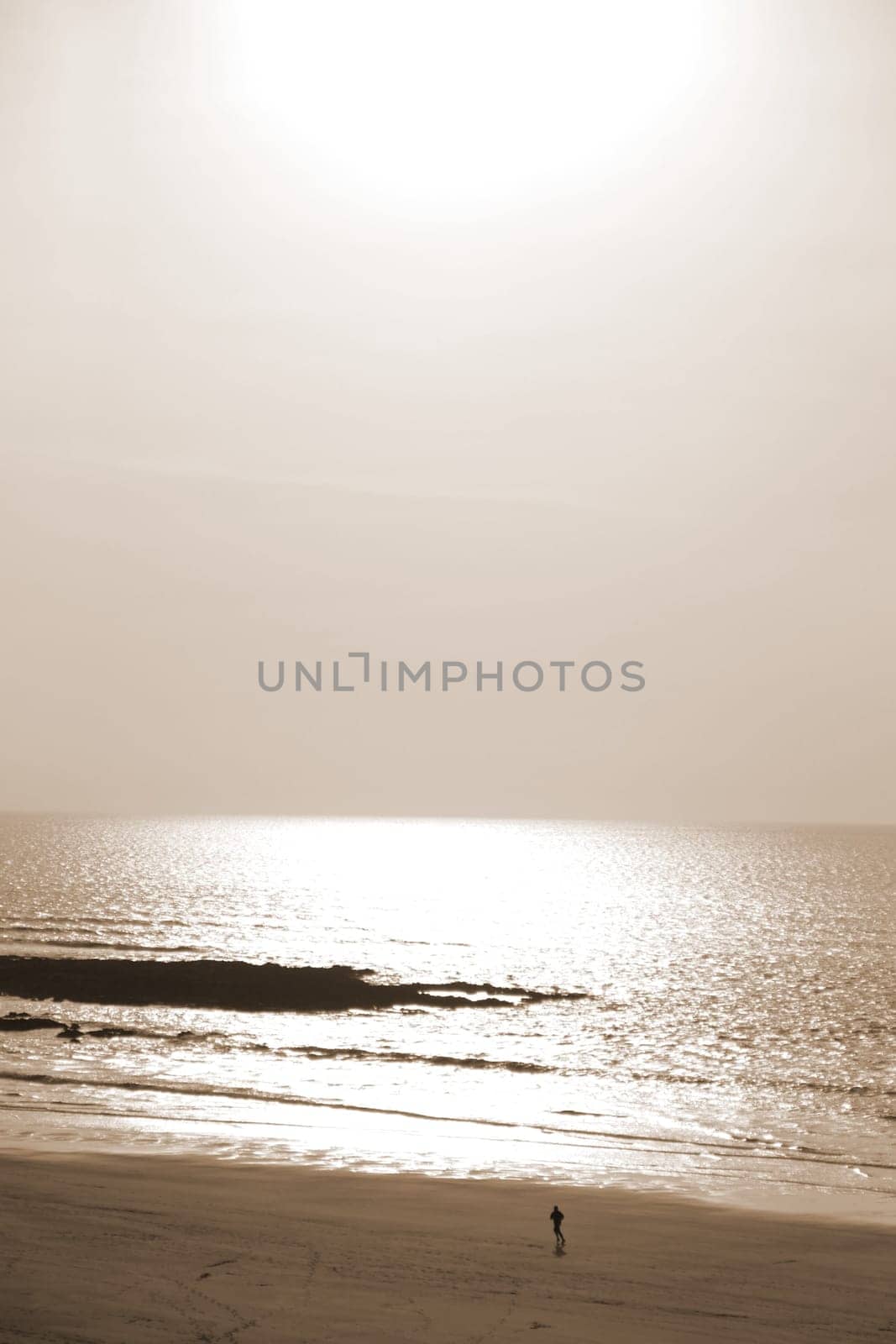 sunshine reflected on a golden beach with jogger of the west coast of ireland in sepia