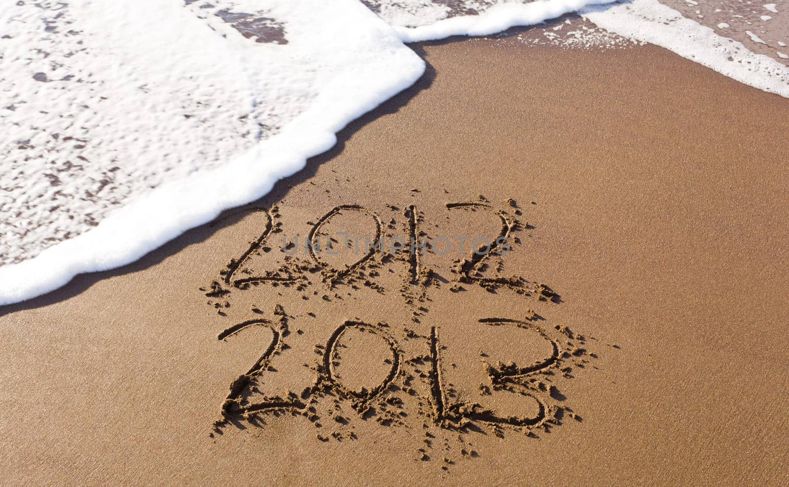 2012 and 2013 written in sand on beach with sea waves starting to erase the word