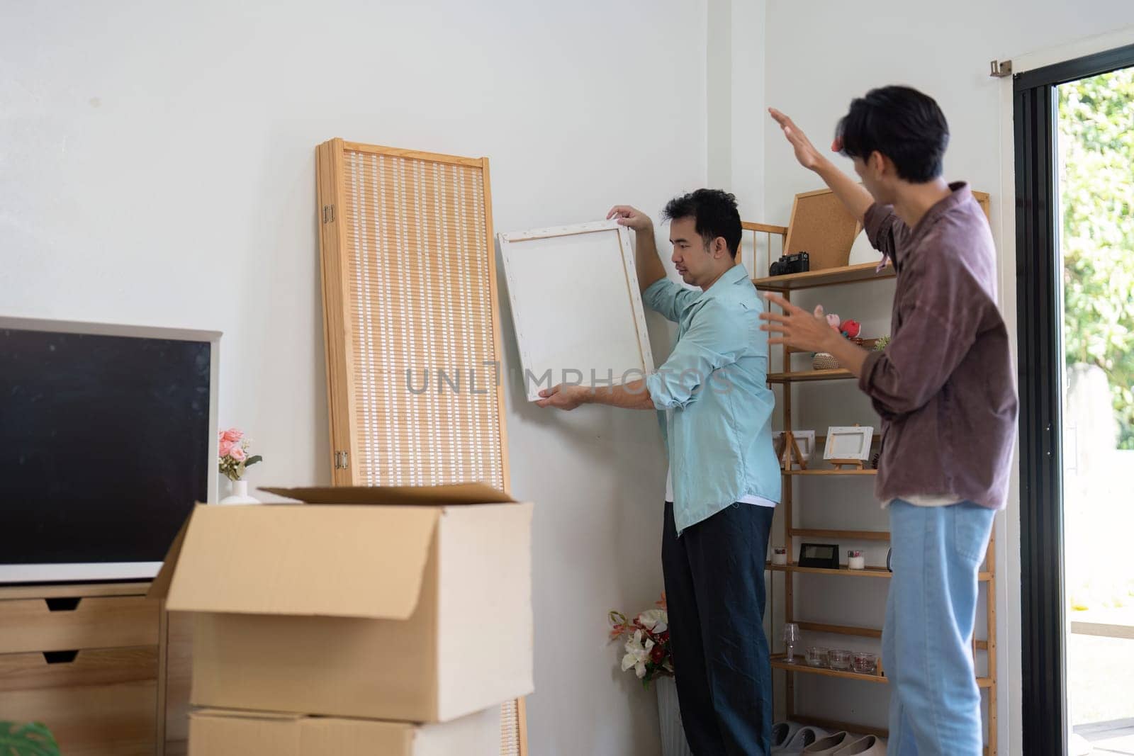 A joyful gay couple unpacks and arranges furniture in their new house, illustrating teamwork and shared joy in their new space.