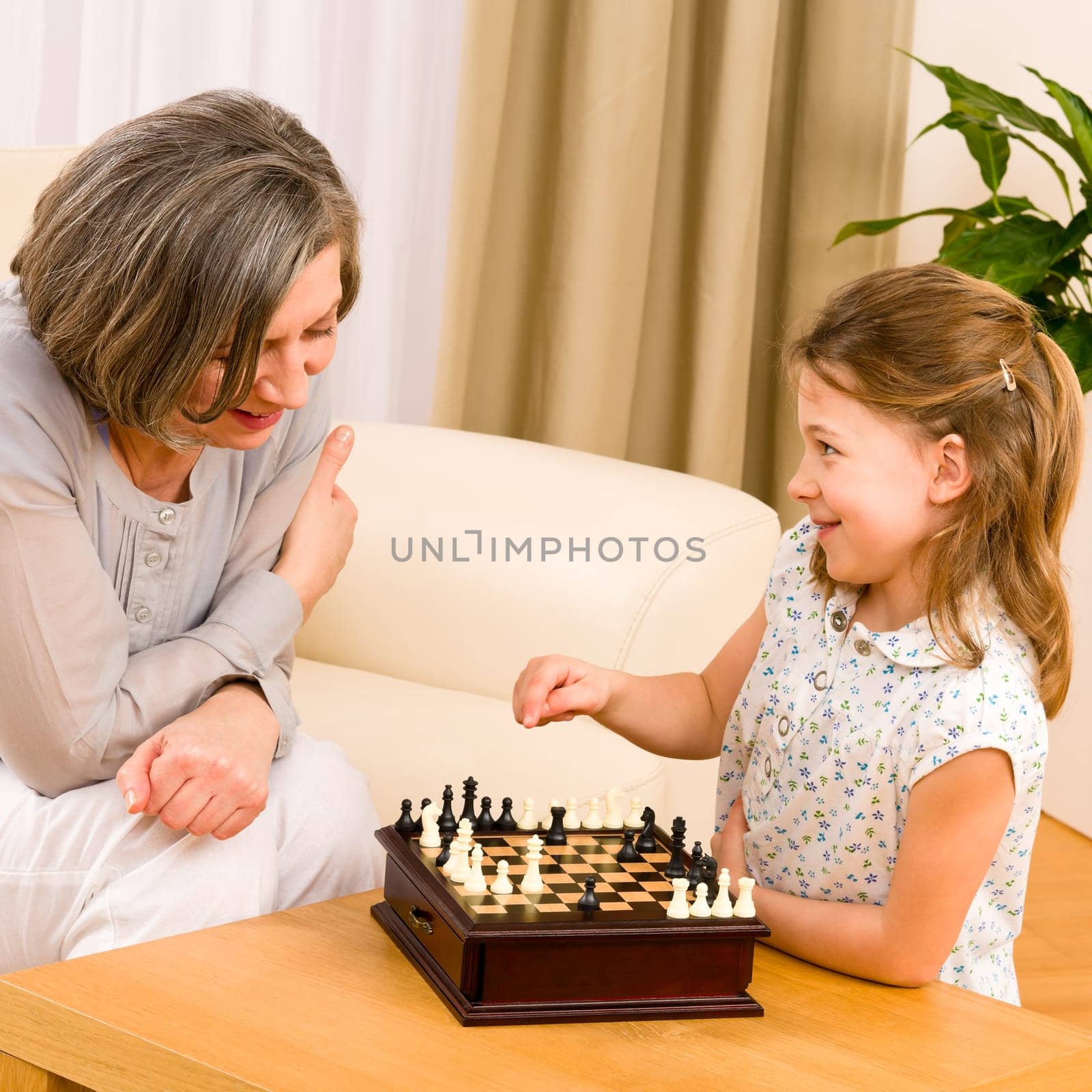 Young girl playing chess with grandmother together at home