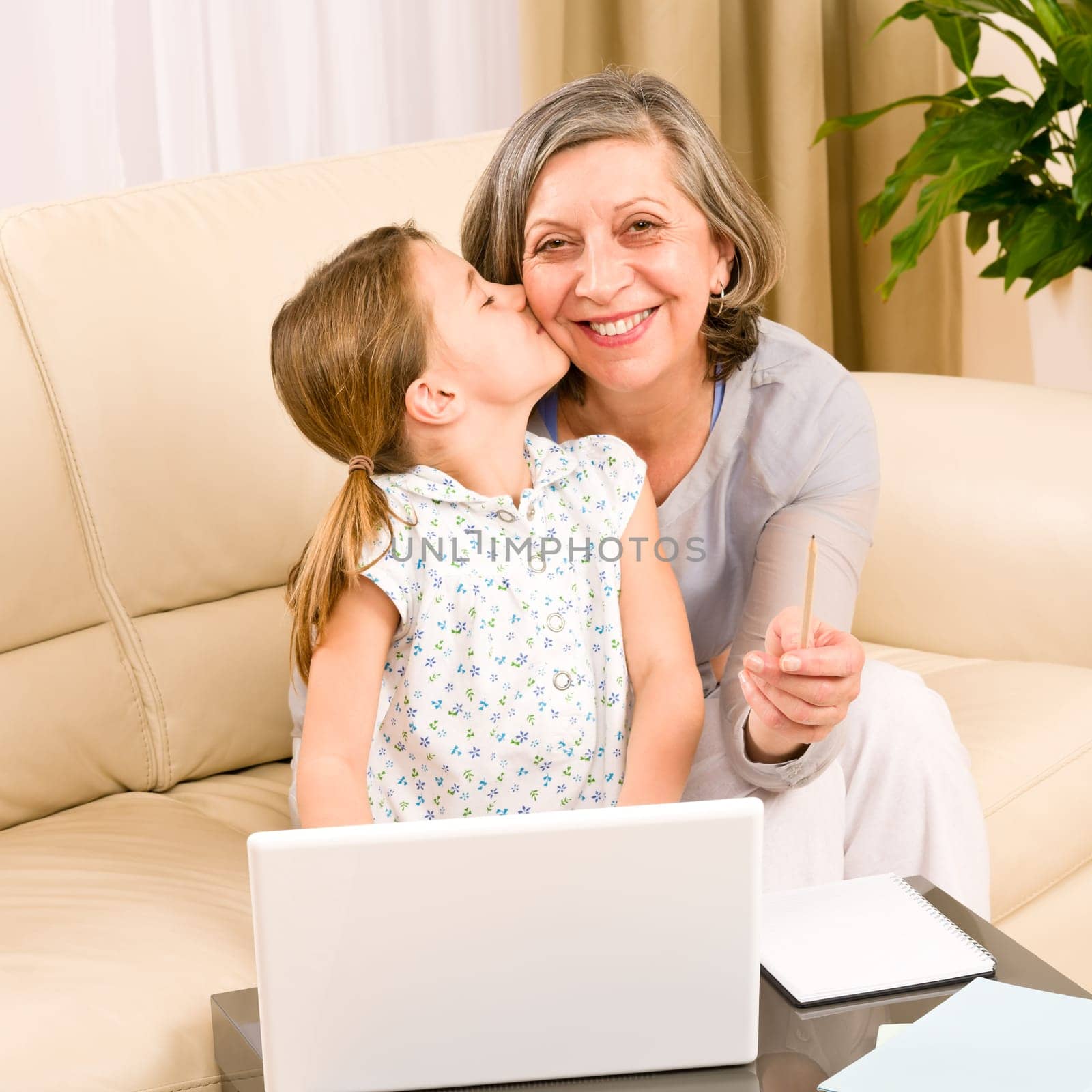 Granddaughter giving kiss to grandmother smiling together on sofa