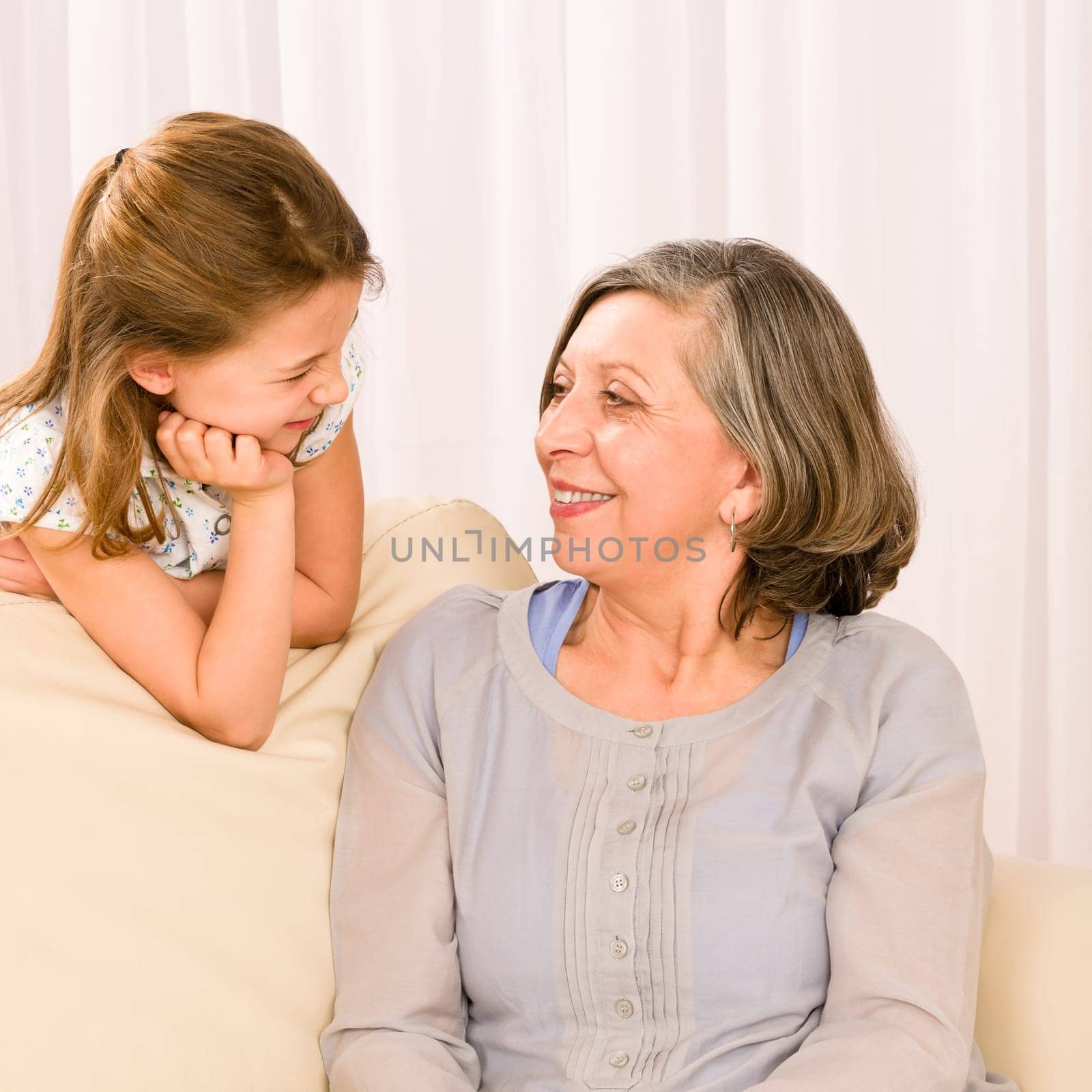 Grandmother and granddaughter look at each other relax on sofa