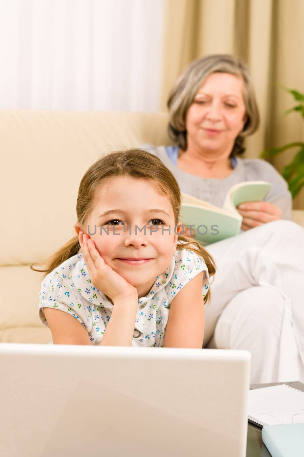 Young girl using computer laptop while grandmother read book at home