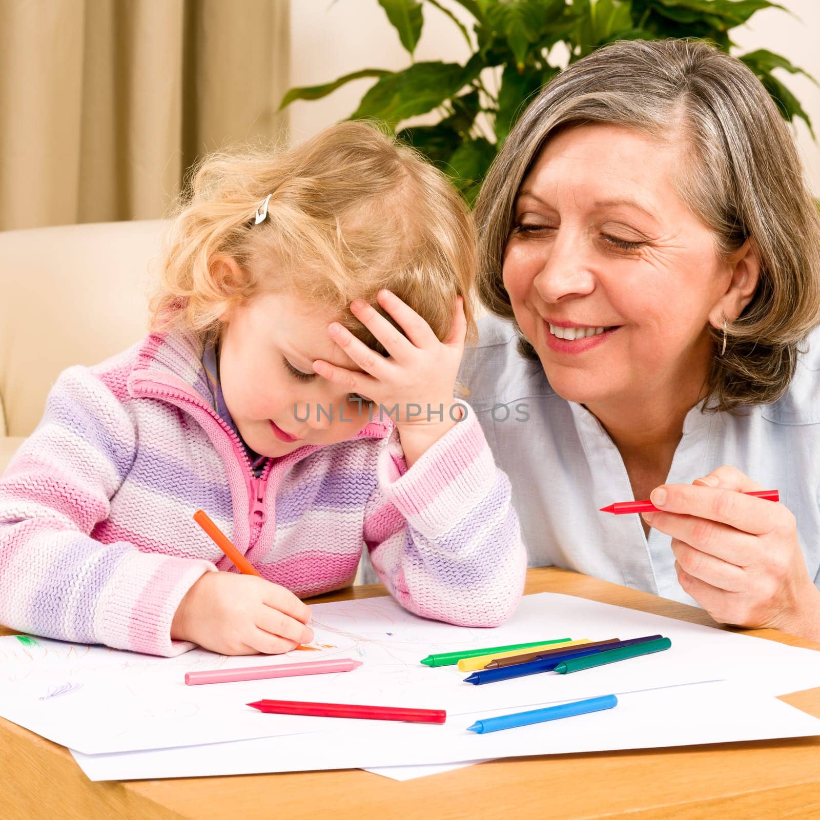Grandmother and granddaughter drawing together with pencils at home