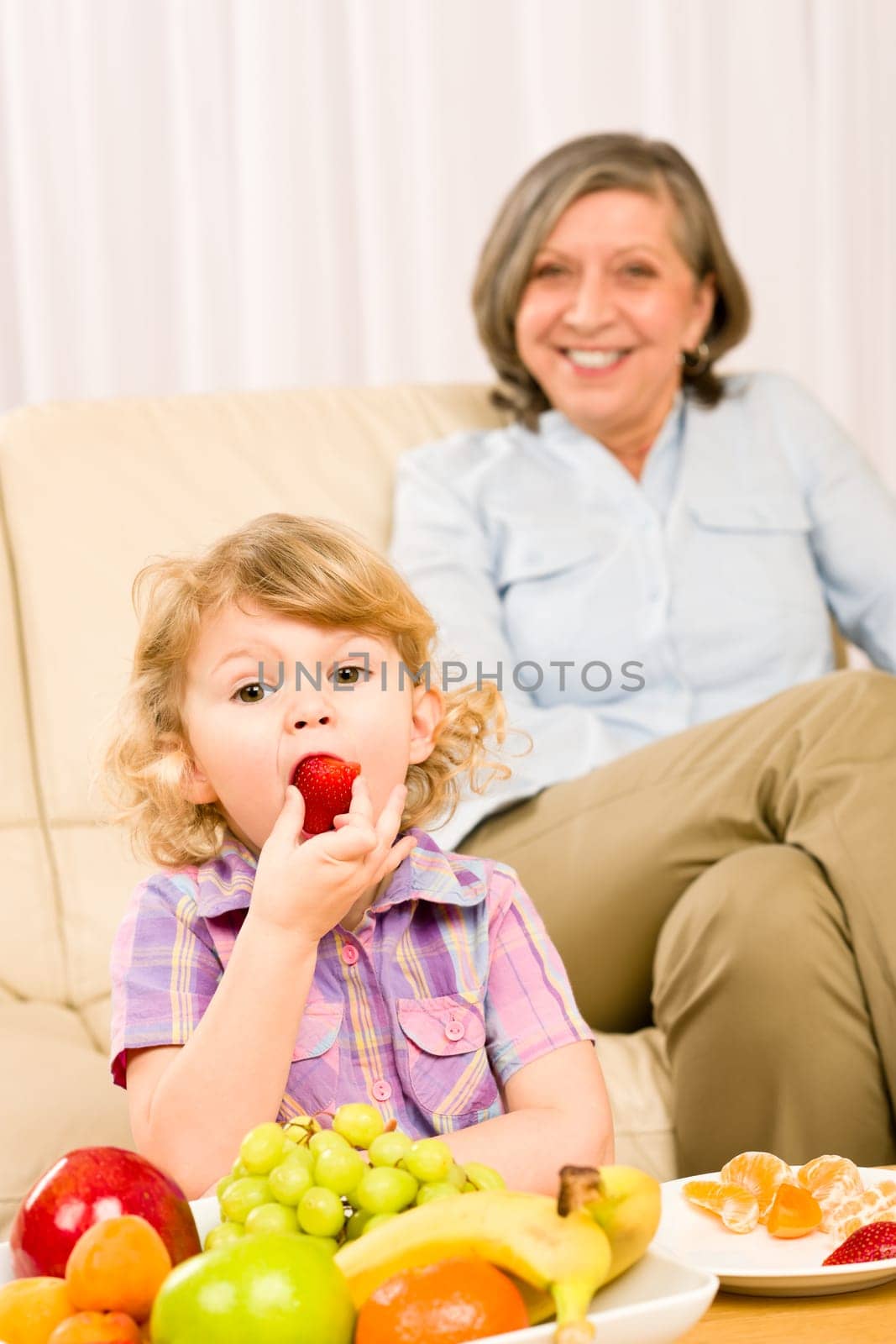 Little girl eat strawberry fruit with grandmother relaxing on sofa