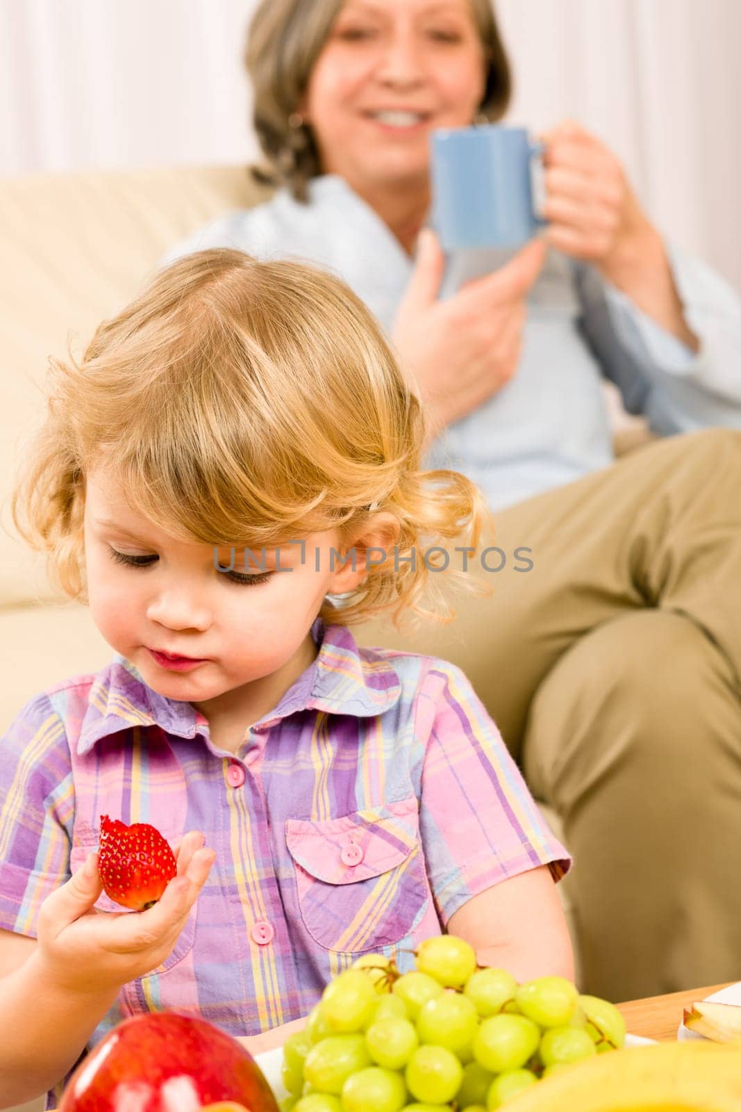 Little girl eat strawberry fruit with grandmother relaxing on sofa