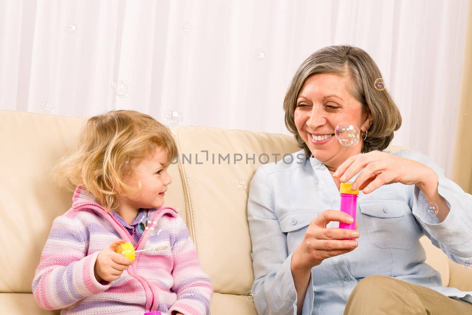 Little granddaughter with grandmother make bubble blower play happy together