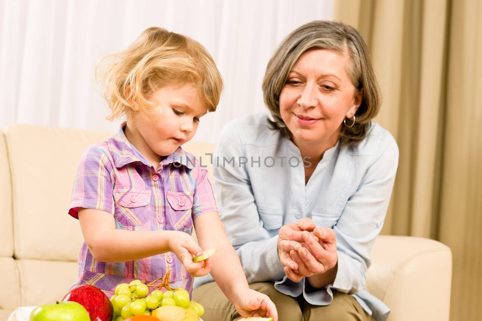 Grandmother with little granddaughter eating fruit happy together at home