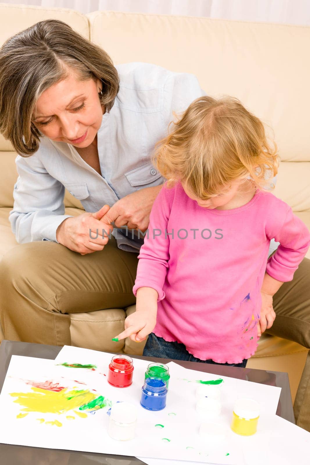 Grandmother with granddaughter playing together paint handprints on paper