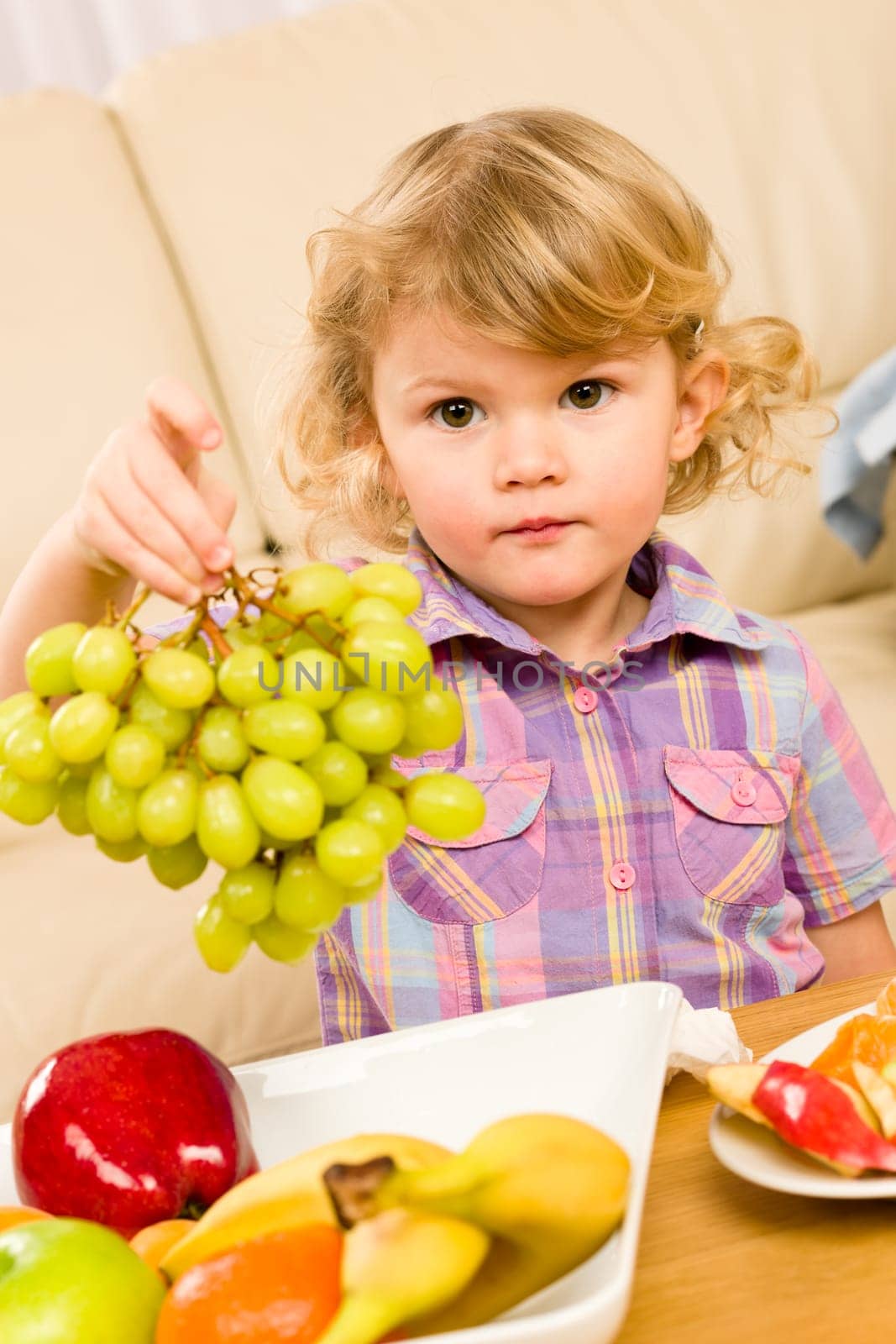 Cute little girl hold grapes healthy fruit bowl at home
