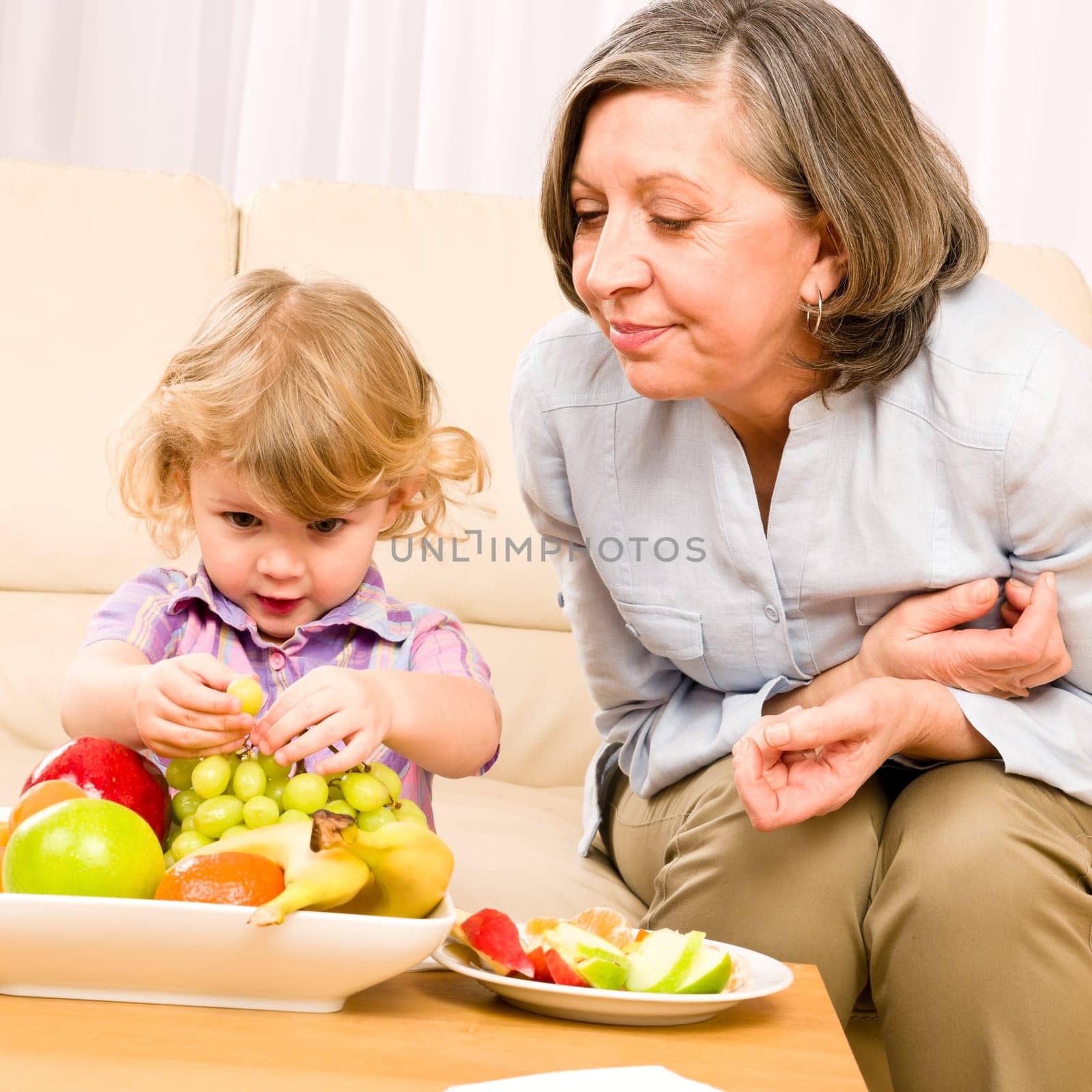 Grandmother with little granddaughter eating fruit happy together at home