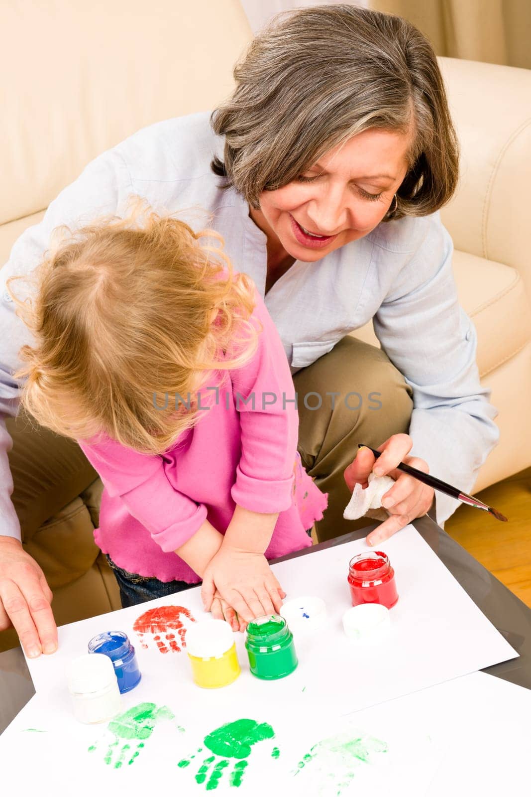 Grandmother with granddaughter playing together paint handprints on paper