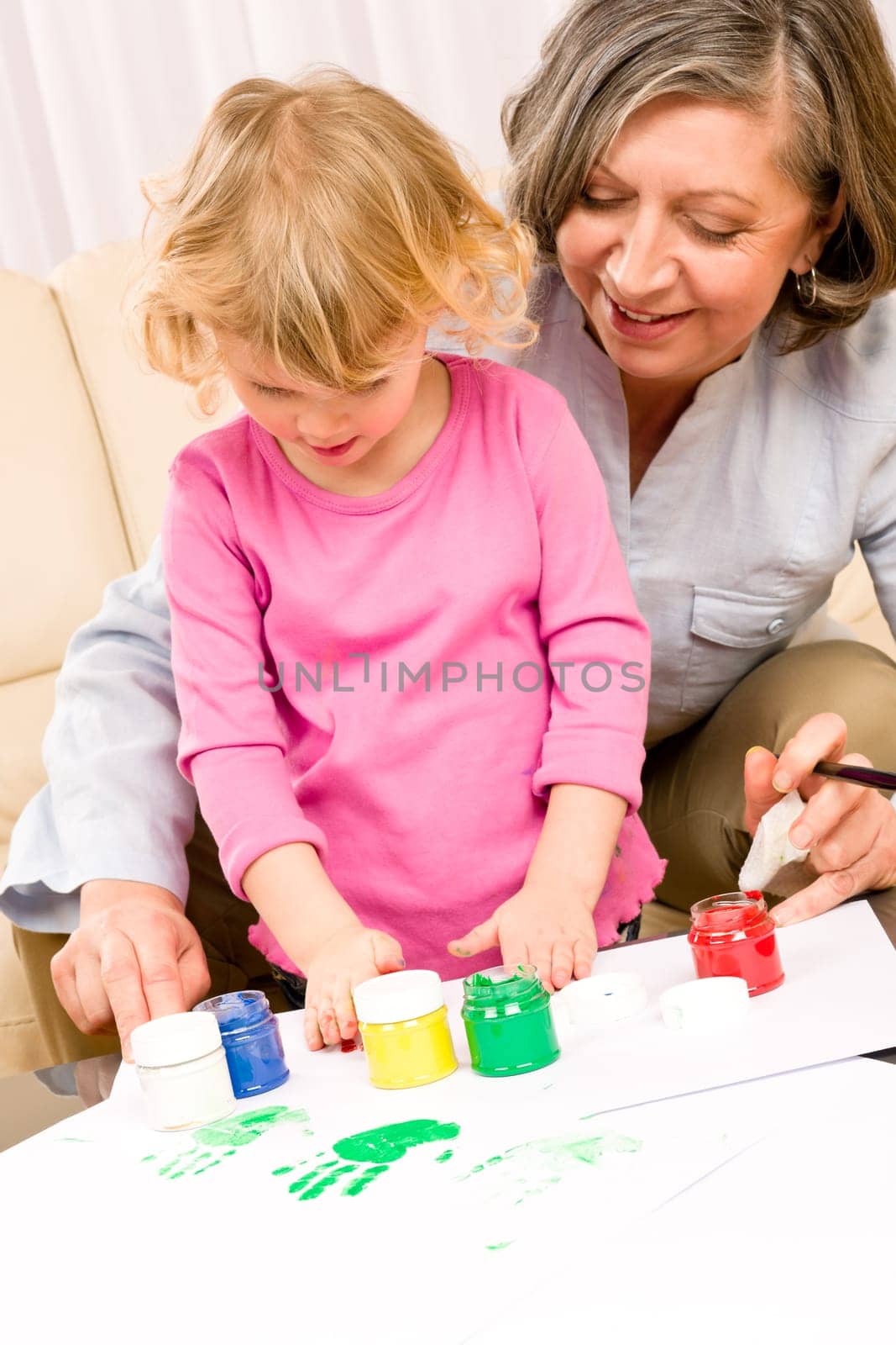 Grandmother with granddaughter playing together paint handprints on paper
