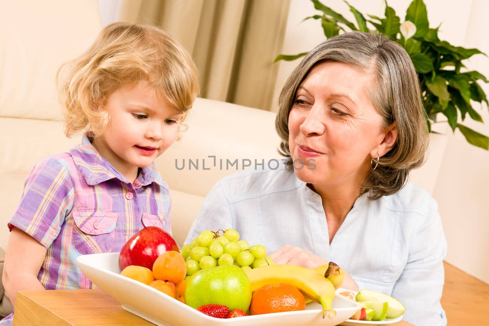 Grandmother with little granddaughter eating fruit happy together at home