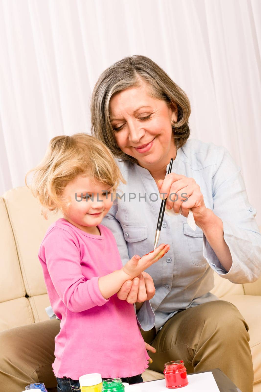 Grandmother with granddaughter playing together paint handprints on paper