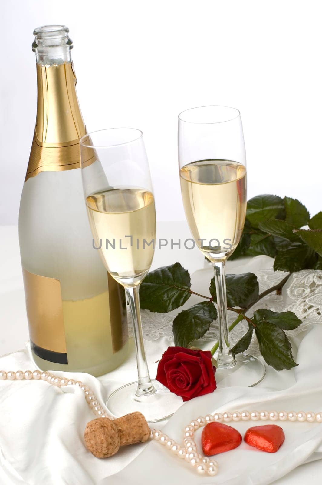 bottle of champagne with two glasses, rose and candy