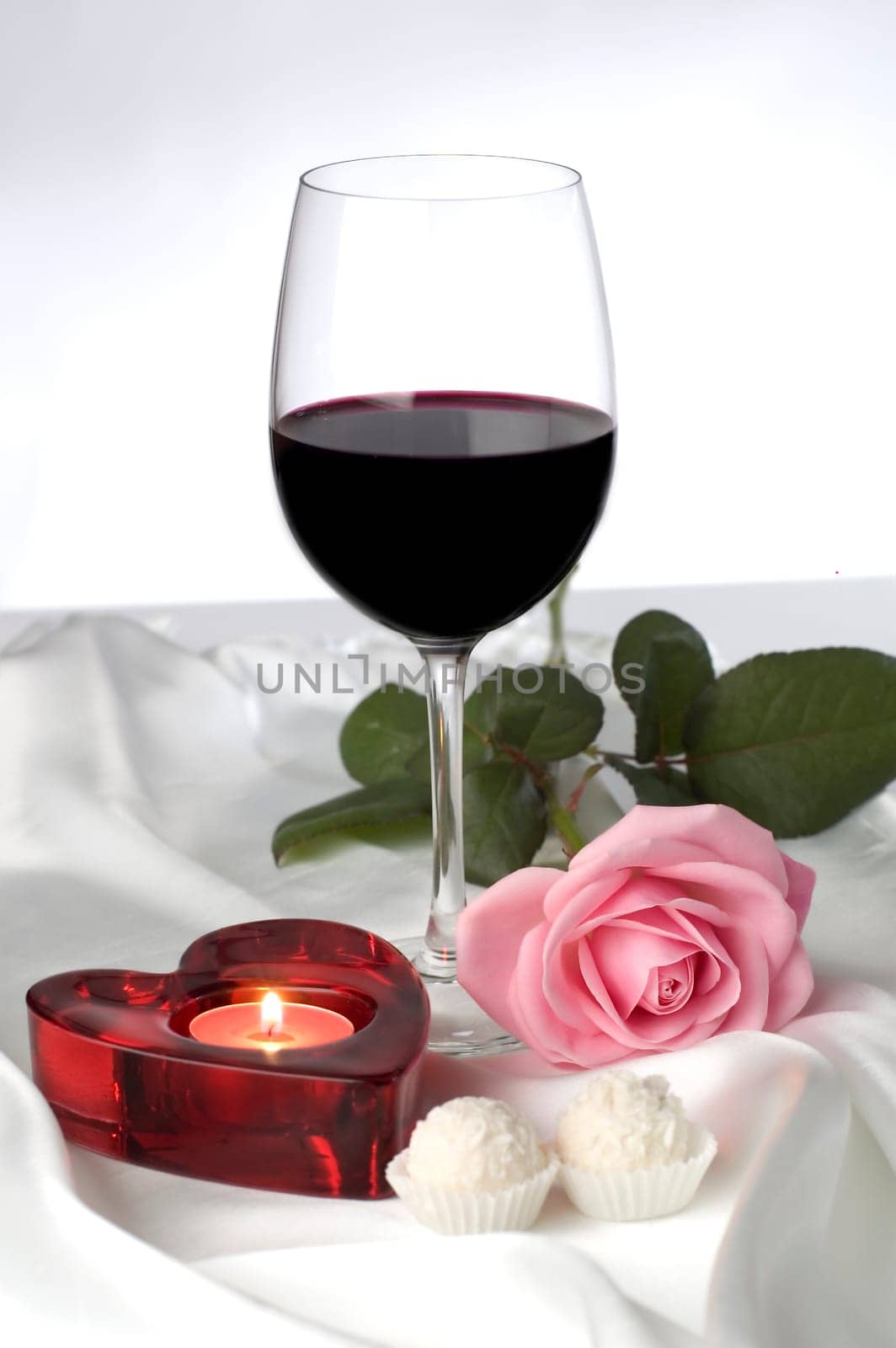 red wine with heart shaped candle on silk close up