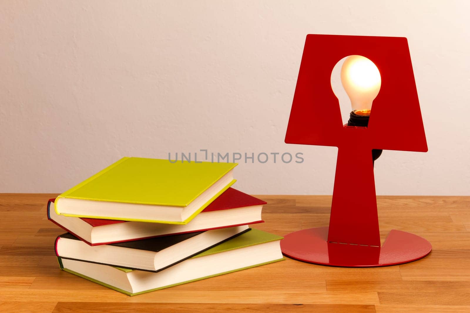 Four books lie on a table,next to them a lamp shines