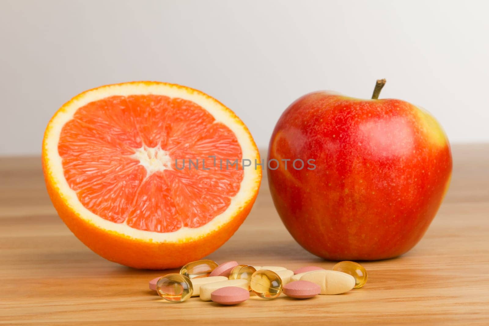 Tablets lie on a table in front of a halved orange and an apple