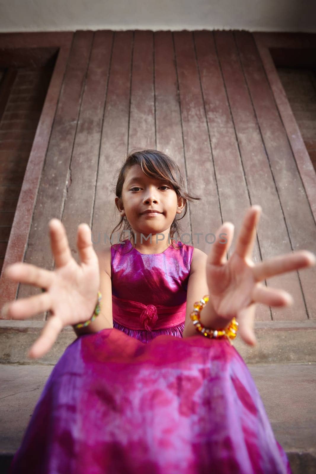 Portrait of cute Asian female child in pink dress pointing hands at camera