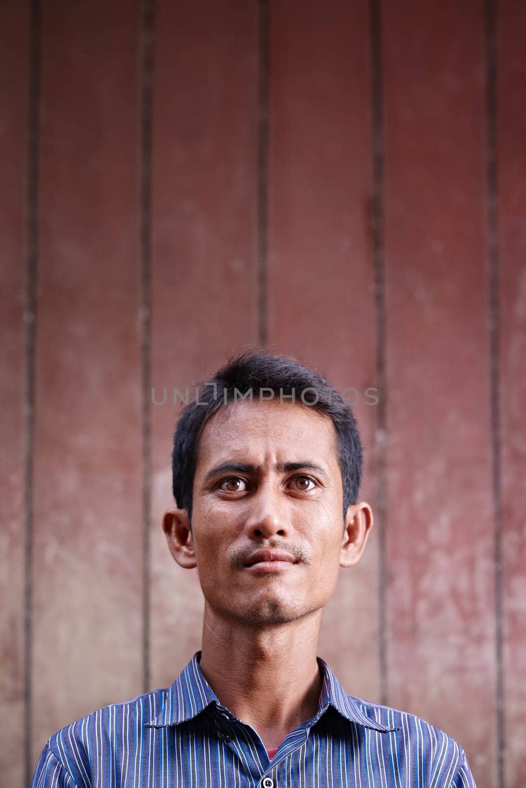 Portrait of mid adult asian man looking up against brown wall. Copy space