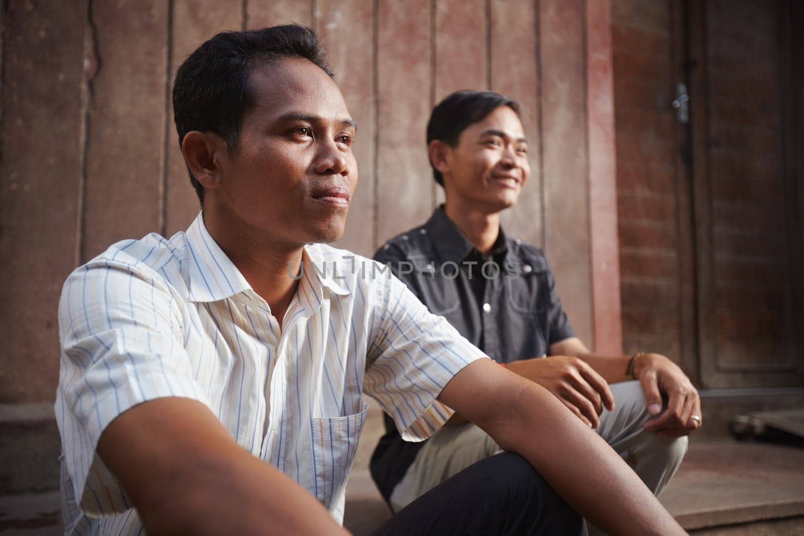 Two male cambodian friends sitting and looking away