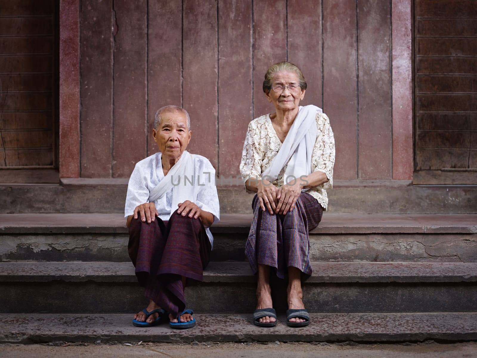 Portrait of two old asian women sitting on steps out of their house and looking at camera