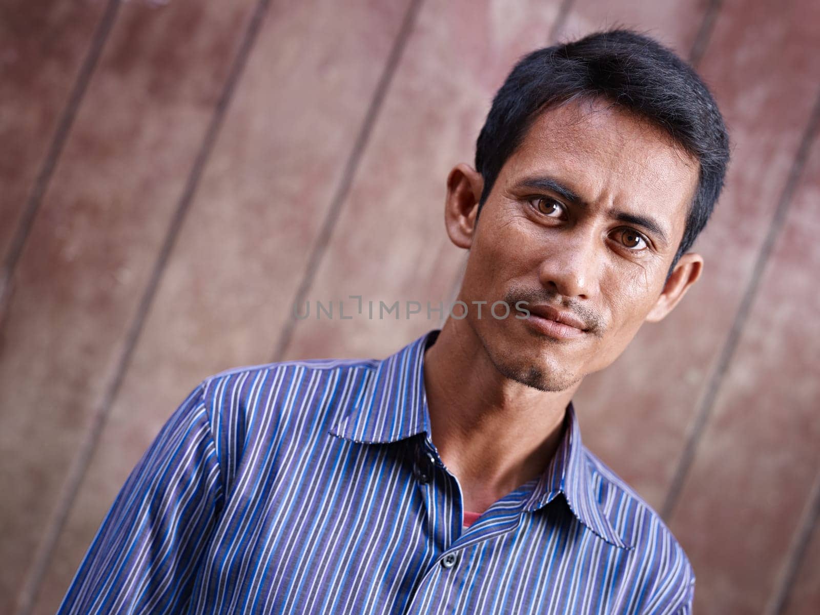 Portrait of mid adult asian man staring at camera against brown wall. Copy space