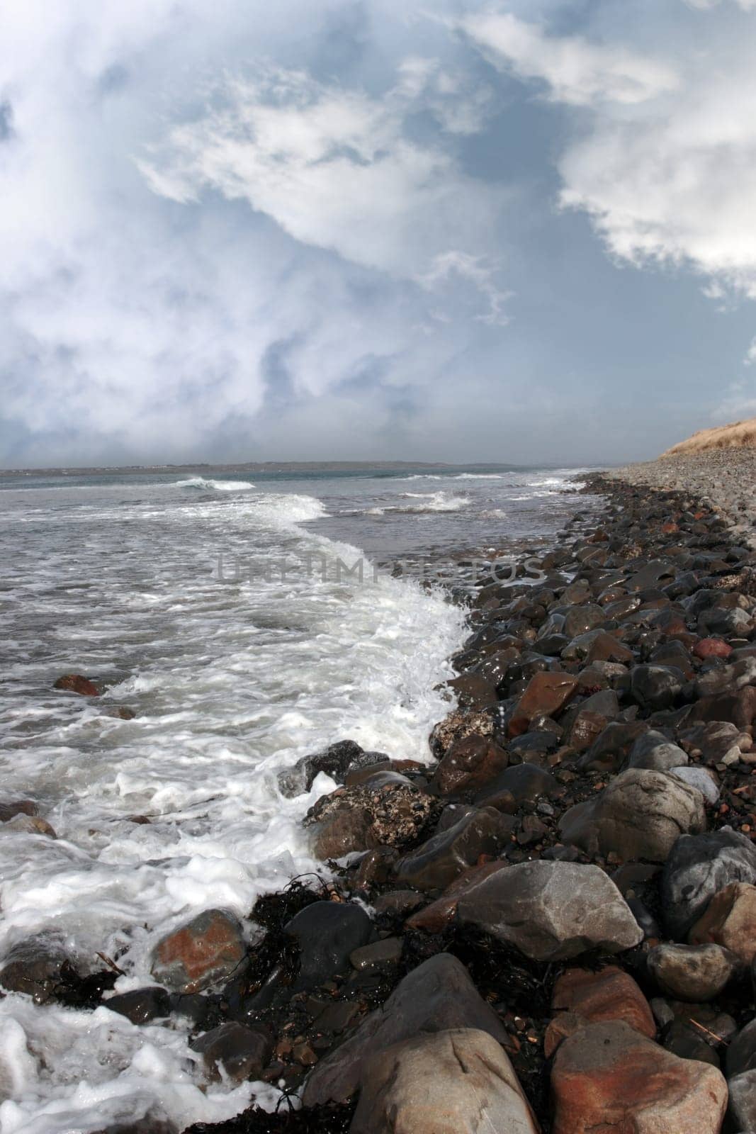 a pebbled beach on a bright day with calm sea waves splashing against the pebbles as a background