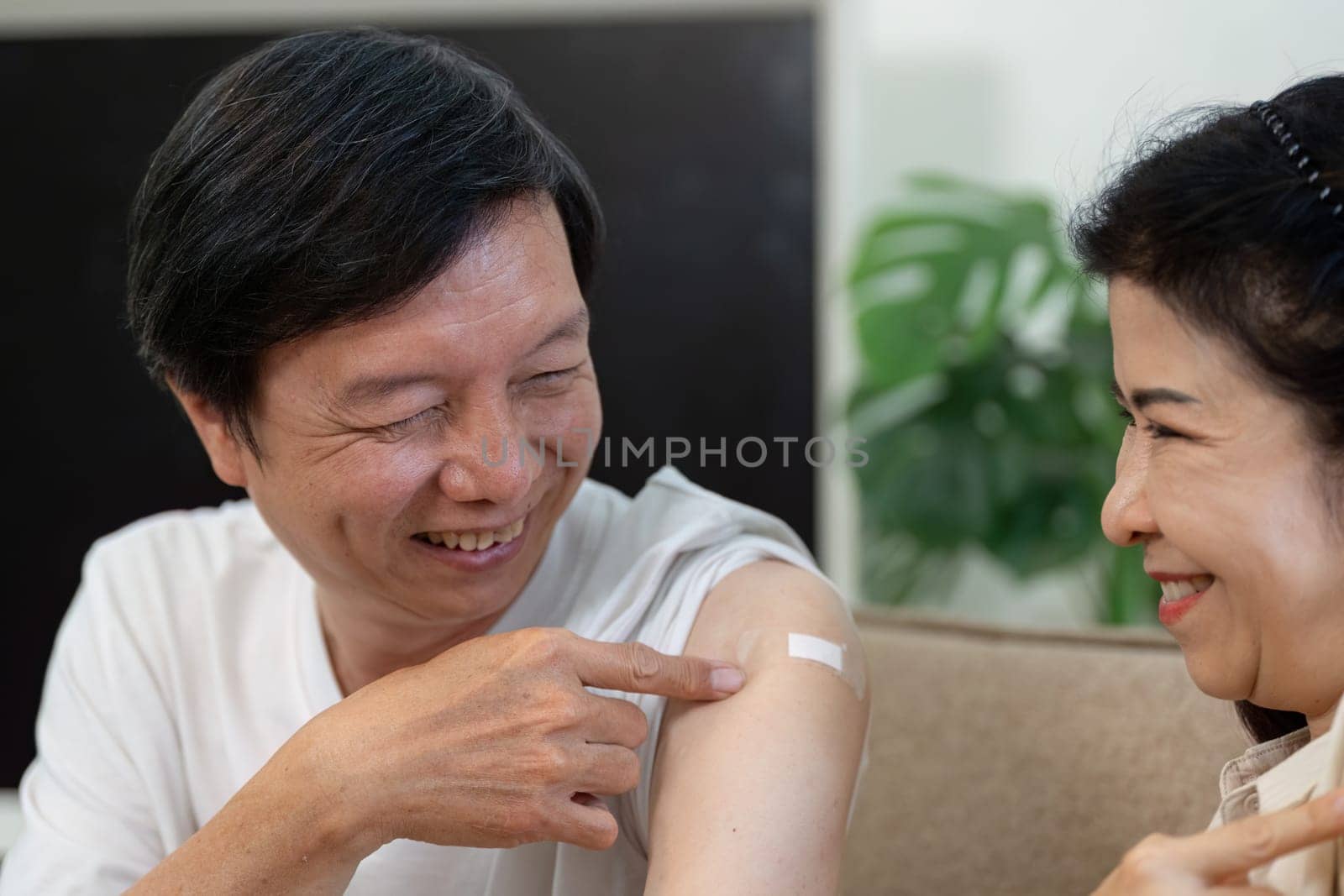 An elderly couple shares a joyful moment, pointing at their vaccination bandages, showcasing support and companionship.