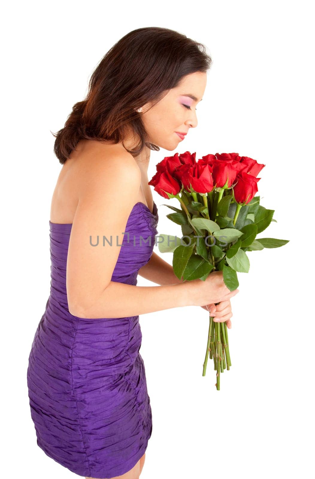 A young woman in an evening dress is holding and smelling roses she just received.