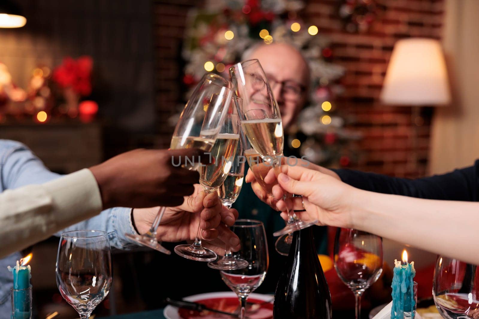 Happy persons clinking glasses at christmas eve festivity, celebrating winter holiday with alcohol and homemade food. Diverse friends and family saying cheers at table, cozy decor.