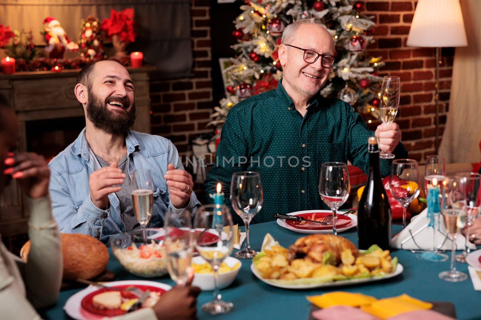 Senior man doing toast with raised glass of wine at christmas eve dinner to celebrate december holiday with friends and family. Grandfather making speech around the table, sparkling alcohol.