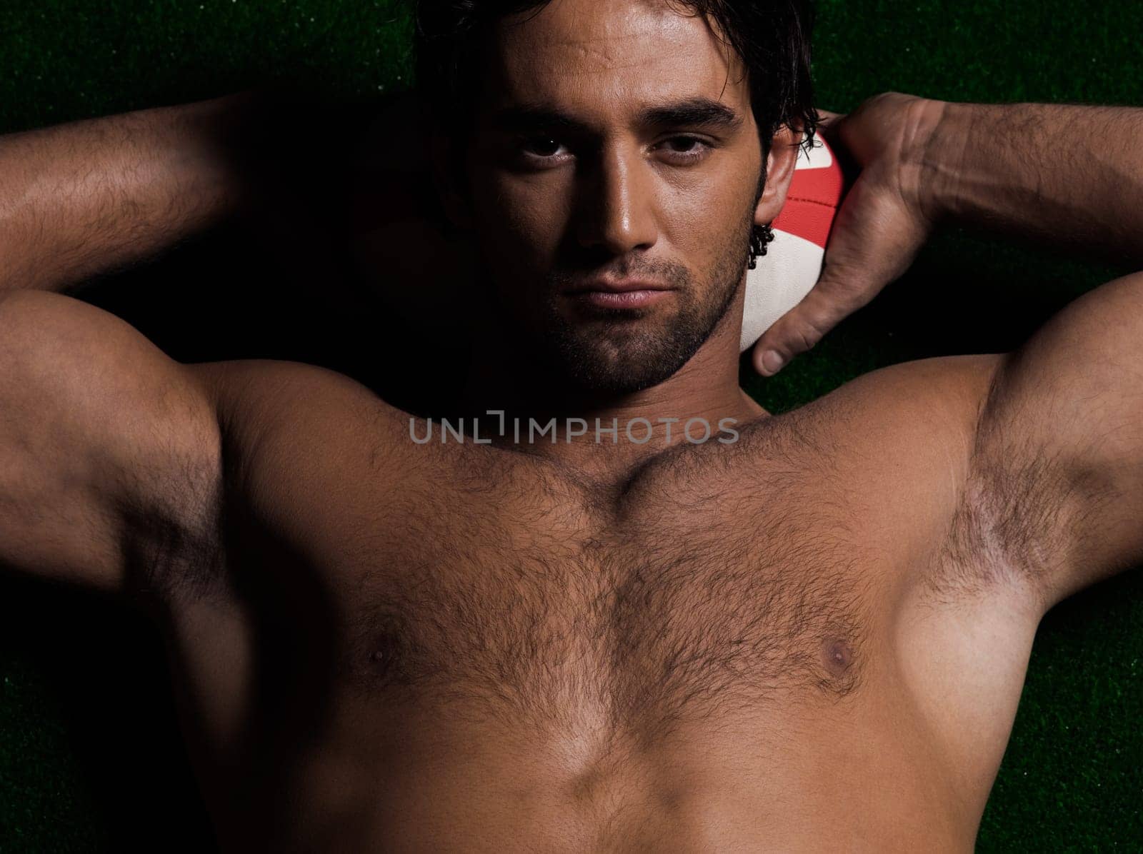 one caucasian sexy topless man portrait hugging a rugby ball on studio black background