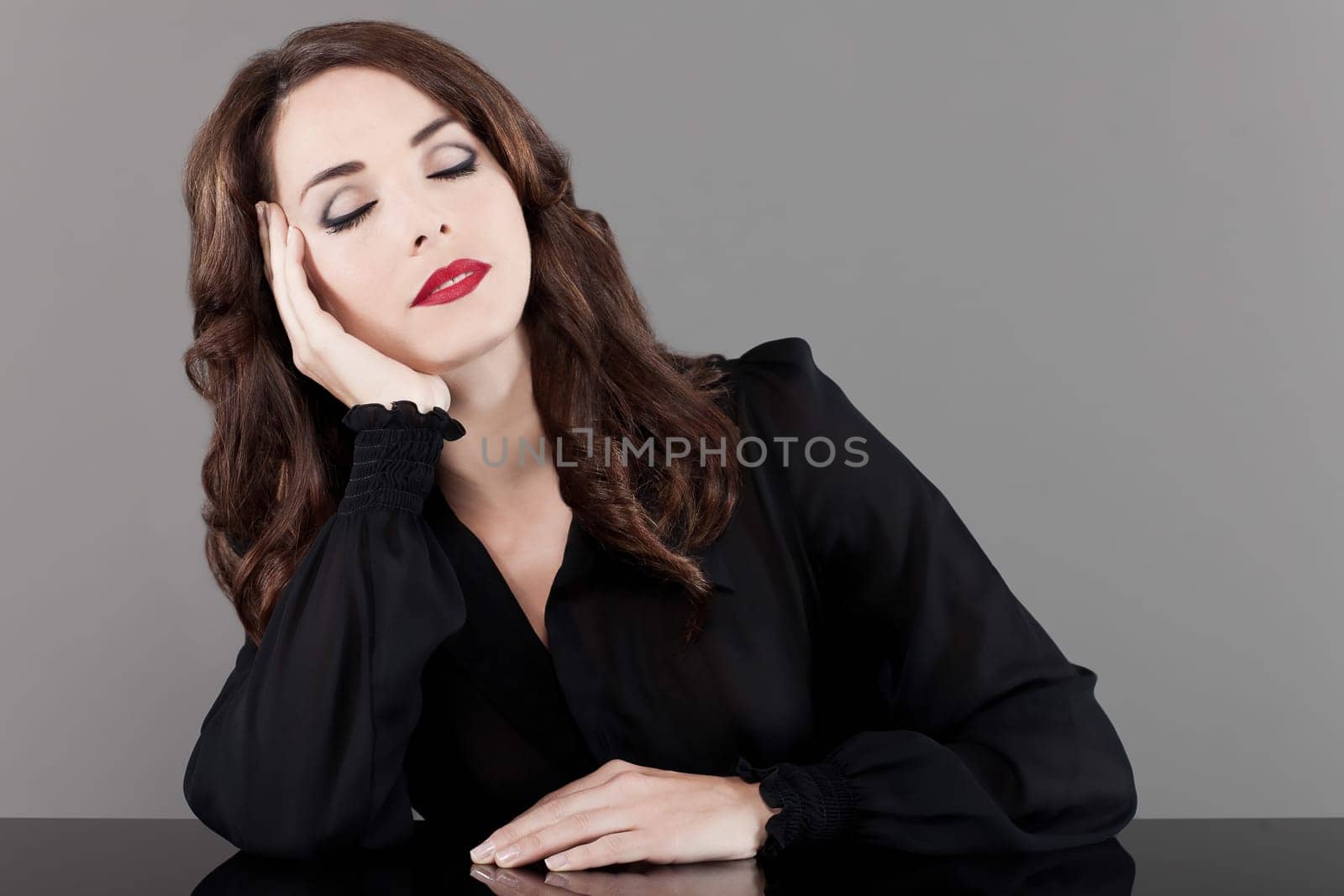 Beautiful middle aged woman sitting at table with eyes closed on gray background