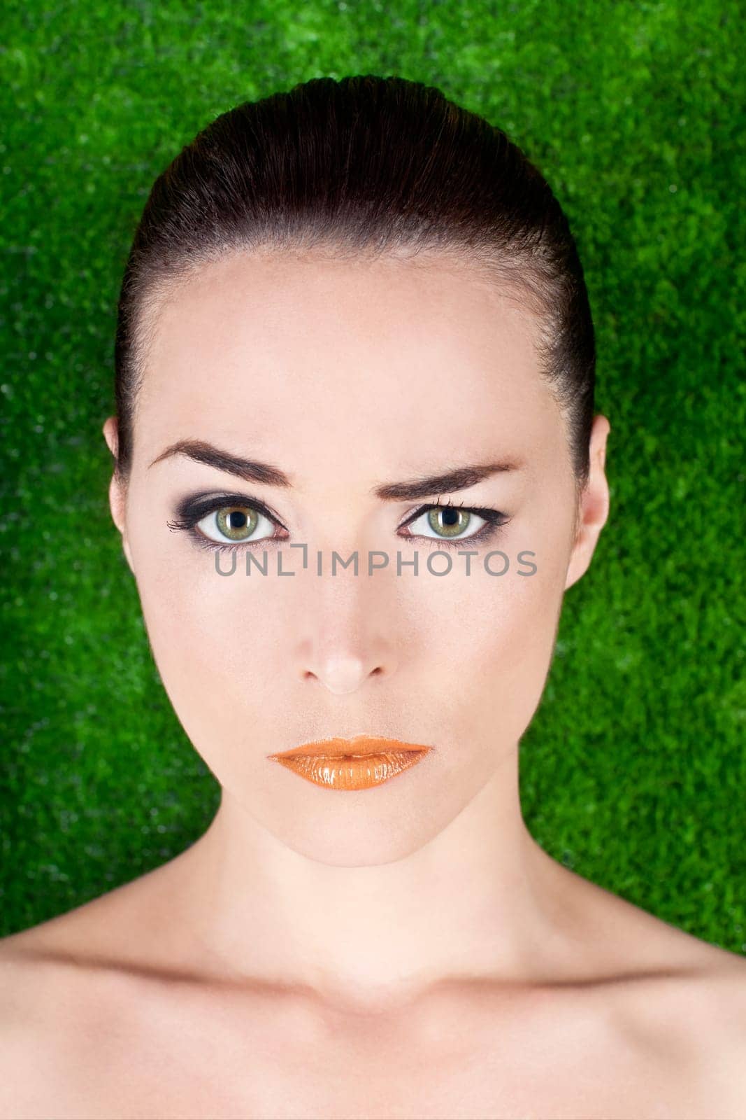 Closeup portrait of a serious beautiful woman raising an eyebrow on green background