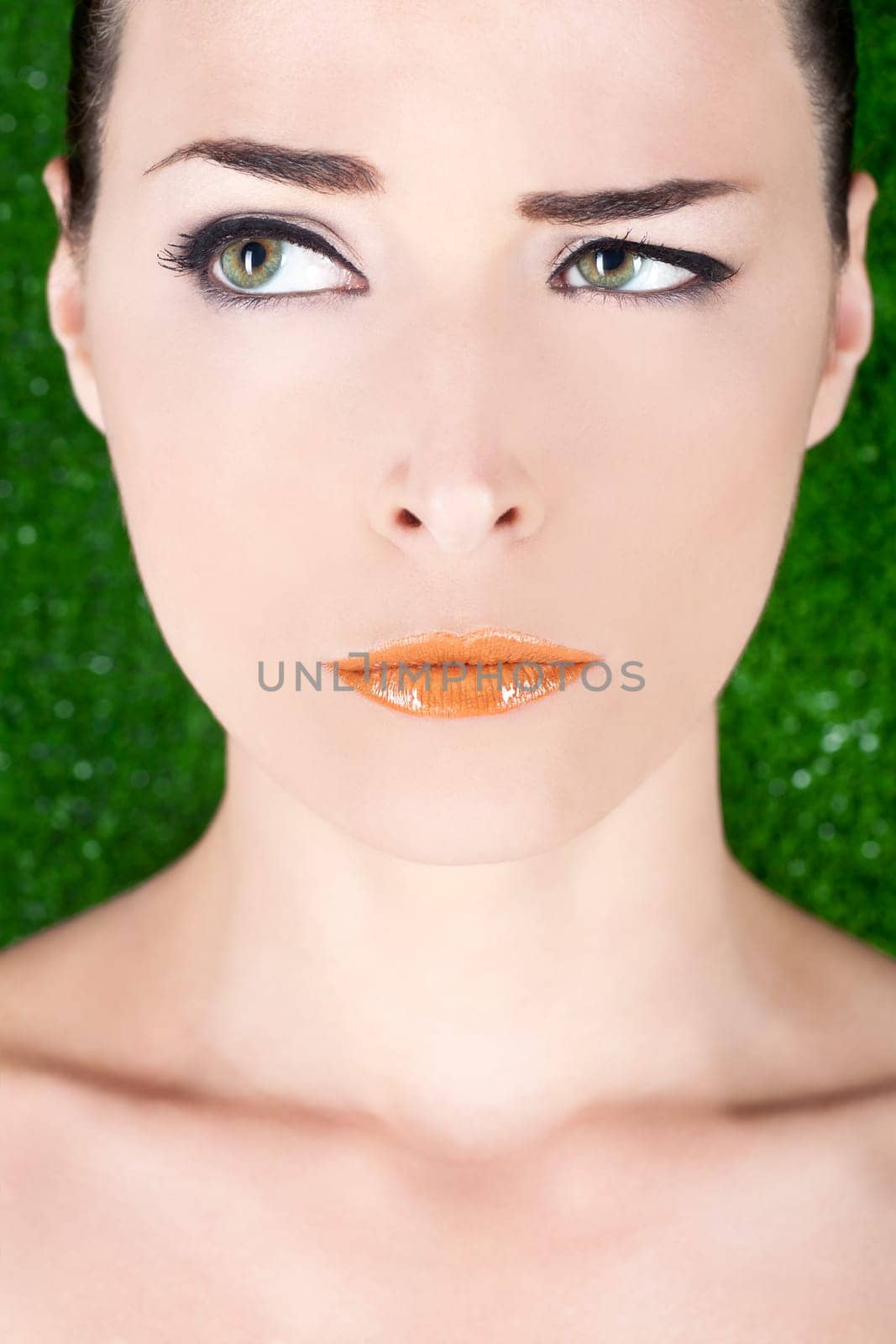 Closeup portrait of a beautiful angry woman with glossy lips looking away on green background