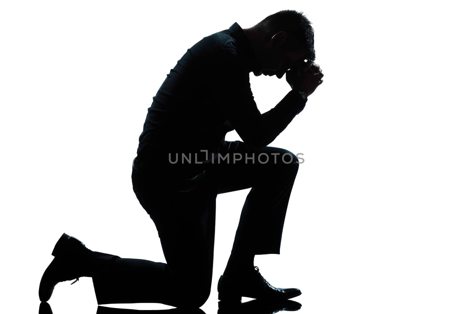 one caucasian man kneeling sadness praying full length silhouette in studio isolated white background