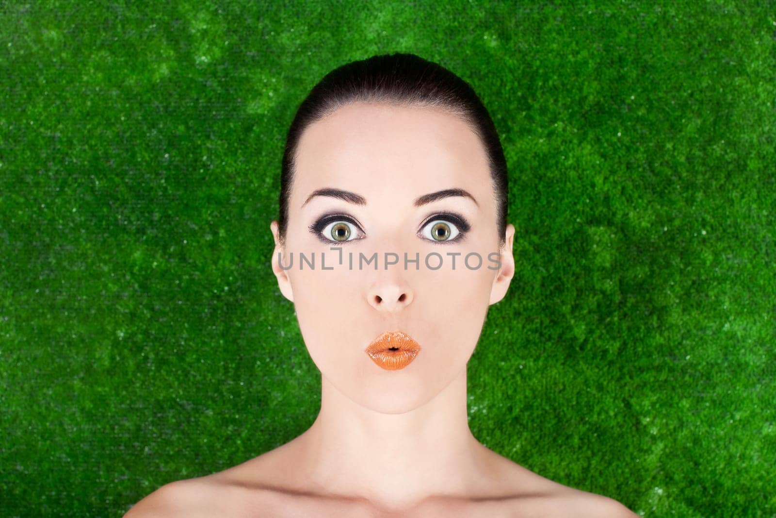 Closeup of a beautiful surprised woman beauty portrait in studio  grass background