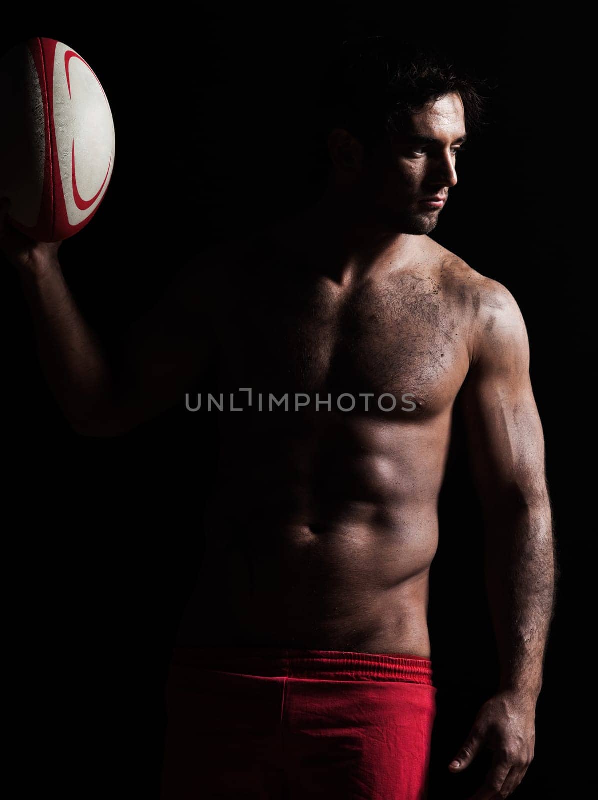 one caucasian sexy topless man portrait holding  a rugby ball on studio black background