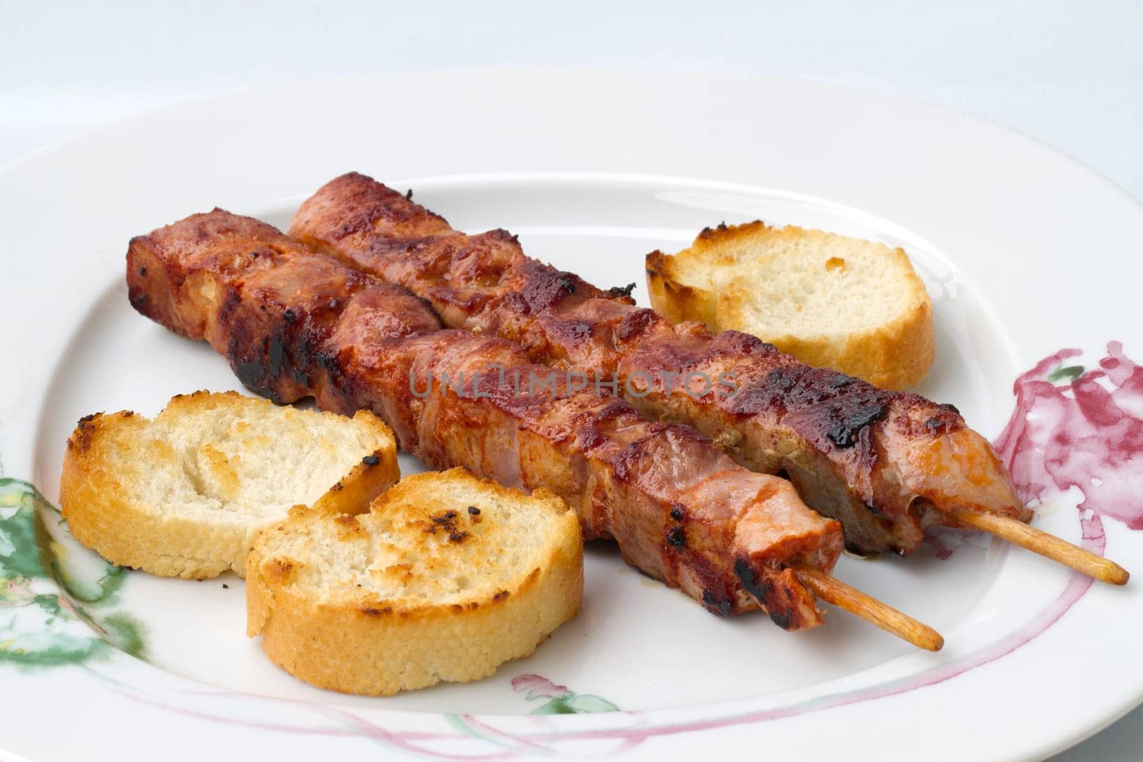 Grilled meat (kebabs) on white plate with three slices of toast